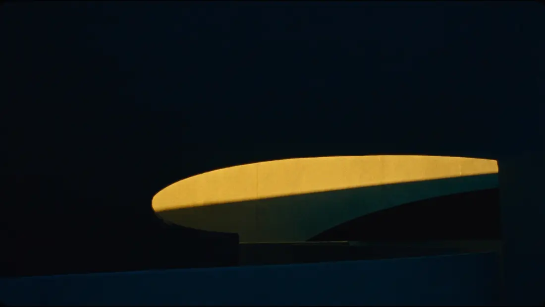 A monumental curved wall in deep shadow, one warm light revealing its arc